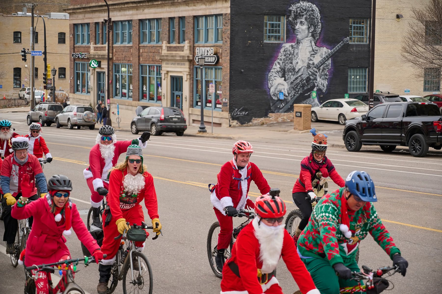 Santa and elf cyclists riding past the Prince mural in Minneapolis